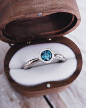 Load image into Gallery viewer, Side view of a bespoke blue diamond solitaire engagement ring that in inspired by the oceans authentic beauty with its hammered band texture and blue colour.