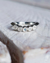 Load image into Gallery viewer, Close up showing a curved wedding ring with five bezels that encase one piece of sea glass and four ocean diamonds. The bezels have a unique rock like texture.
