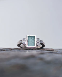 Close up of rare sea glass handcarved into a rectangle and set in 18ct white gold. This engagement ring has an art deco theme and has a total of 6 diamonds flanking the sea glass.