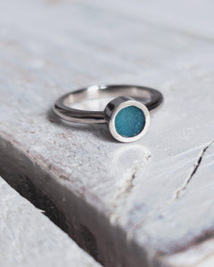 Close up of a bespoke MERMAID engagement ring which features teal sea glass, set within our signature flat topped bezel.