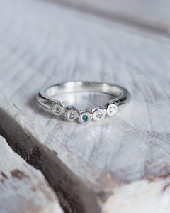 Front view of a beautiful sterling silver wedding ring that has five bezel settings with teal sea glass and ocean diamonds set within.