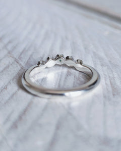 Close up showing the curve of the wedding ring that is designed to flow around the setting of an engagement ring. This design has one piece of sea glass and four diamond in bezel settings.